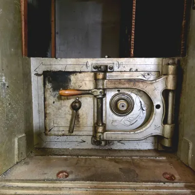 Antique heavy steel safe compartment with intricate hand-painted scrollwork, a combination dial, and heavy locking lever mechanisms.