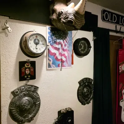 Sale Photo Thumbnail #17: Eclectic wall display featuring a Hornsby's rhinoceros head mount, vintage Soviet CCCP metal plaques, a submarine-style wall clock, and a black rotary wall telephone.