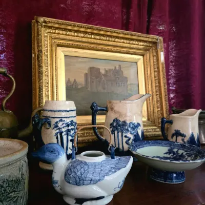 Collection of vintage blue and white ceramics, including a duck-shaped teapot, pitcher set, and pedestal bowl, displayed in front of a...