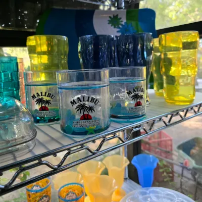 Assorted vintage plasticware, including Malibu Rum branded tumblers with liquid-filled double walls and colorful plastic cups, displayed...