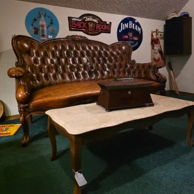 Ornate tufted brown leather sofa with carved wood trim, paired with a marble-top coffee table and a vintage wooden box.