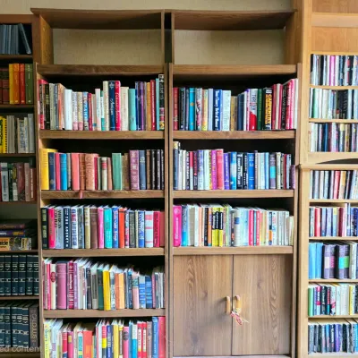 Large collection of hardcover and paperback books organized across multiple wooden bookcases, including fiction, reference, and...