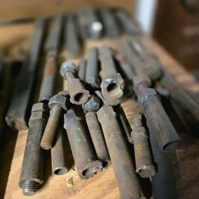 Sale Photo Thumbnail #41: Assortment of vintage rusted metal bolts, pipes, and threaded rods on a wooden workbench.