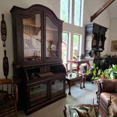 Large dark wood roll-top secretary desk with a glass-front upper cabinet and lower bookcase, shown alongside carved tables and additional...