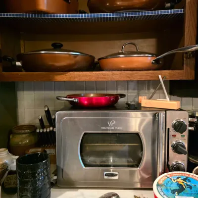 Stainless steel Wolfgang Puck countertop oven surrounded by copper-toned cookware, kitchen utensils, and decorative serving items.