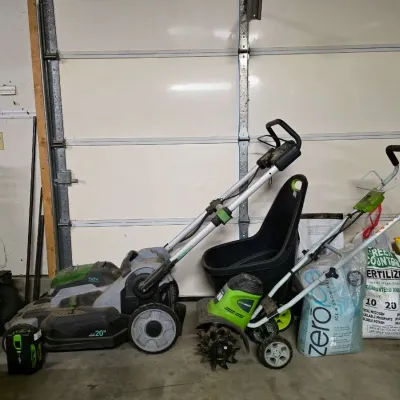 EGO 56V cordless 20-inch lawn mower with battery and a Greenworks electric tiller/cultivator, accompanied by bags of lawn fertilizer and...