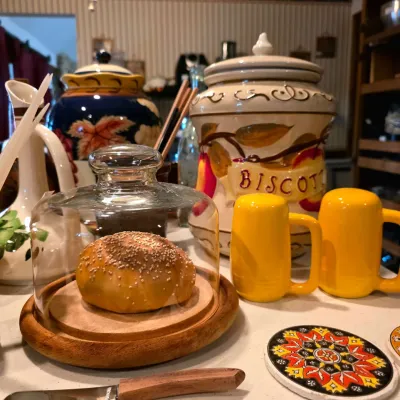 Collection of vintage kitchenware including a wooden-base cloche with a decorative bread model, yellow ceramic mugs, a hand-painted...
