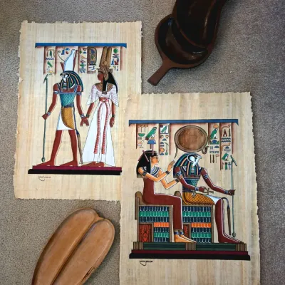 Sale Photo Thumbnail #49: Two hand-painted Egyptian papyrus art pieces depicting deities, shown alongside two vintage carved wooden leaf-shaped serving dishes.