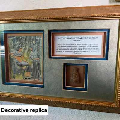 Sale Photo Thumbnail #54: Framed decorative replica of an Egypt-Roman head fragment, featuring an informational plaque, an illustration, and a small clay head replica in a shadow box frame.