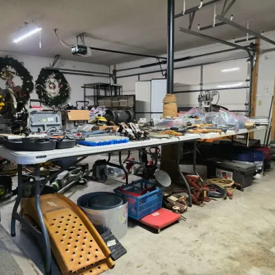 Assortment of power tools, hand tools, and workshop equipment displayed on folding tables in a garage, including a miter saw, hand...