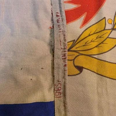 Sale Photo Thumbnail #32: Close-up of a vintage Soviet-era flag or banner showing a printed date of 1985 on the fabric edge, with some wear and minor staining.