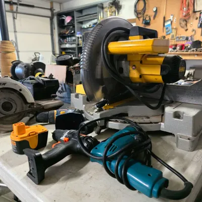 Sale Photo Thumbnail #38: Assorted power tools including a DeWalt miter saw, a Skilsaw circular saw, a Makita corded drill, and a cordless drill with battery pack, showing signs of regular workshop use.