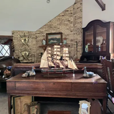 Antique wooden piano table or desk featuring a detailed model sailboat, wooden duck decoys, framed artwork, and a small wooden chest...