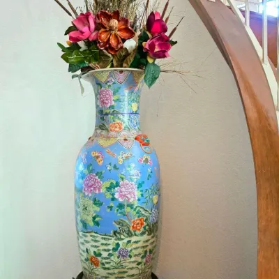 Large Chinese light blue floor vase featuring floral and butterfly motifs, displayed on a dark wooden carved stand and filled with...