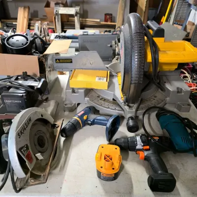 Sale Photo Thumbnail #37: Assortment of power tools including a DeWalt miter saw, a Skilsaw circular saw, a Craftsman belt sander, and various cordless drills with a battery pack.