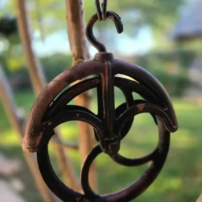 Vintage cast iron well pulley with a hanging hook, showing a weathered dark finish and rustic patina.