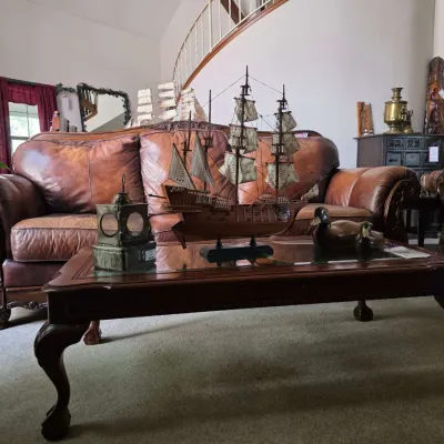Queen Anne style wood coffee table displaying a model sailing ship, decorative lantern, and duck figurines in front of a brown leather sofa.