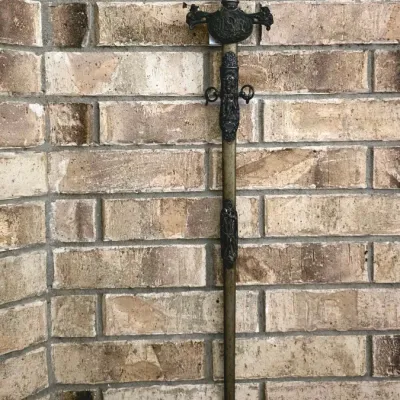 Antique fraternal sword with detailed metal hilt and matching ornamental scabbard, displayed against a brick wall.