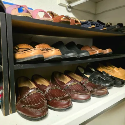 Collection of men's and women's vintage leather footwear, including loafers and sandals, neatly displayed on wooden shoe racks...