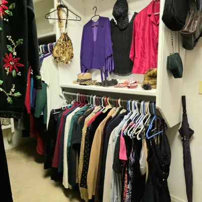 Walk-in closet filled with women's clothing, including jackets, blouses, sequined accessories, purses, and hats.