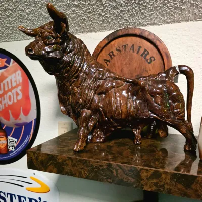 Vintage ceramic bull figurine with a glossy brown glaze, displayed on a shelf alongside bar memorabilia.