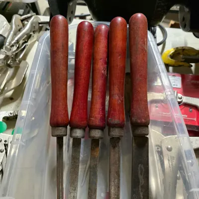 Sale Photo Thumbnail #53: Set of five vintage woodturning chisels with reddish-brown wooden handles, showing signs of wear and surface rust on the metal blades.