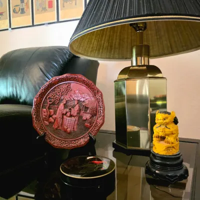 Collection of Asian-inspired decor including a carved red cinnabar-style plate on a stand, a small yellow foo dog figurine, a black...