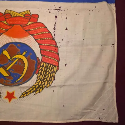 Sale Photo Thumbnail #26: Vintage Soviet-era flag featuring the State Emblem of the Soviet Union, showing some staining and wear on the white fabric.