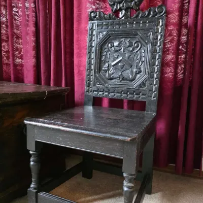 Sale Photo Thumbnail #11: Antique dark-stained oak hall chair featuring an elaborately carved backrest with a central crest motif, turned front legs, and a decorative finial.