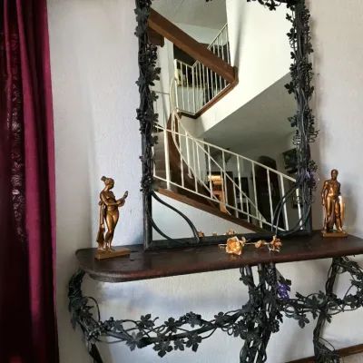 Large wrought iron console table and matching wall mirror with intricate grapevine and leaf metalwork, flanked by small metallic figures.
