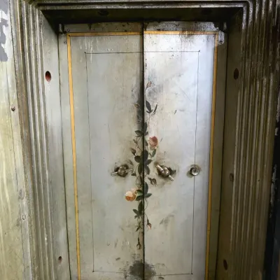 Antique iron vault double doors featuring hand-painted floral motifs and dual turn handles inside a heavy molded frame.
