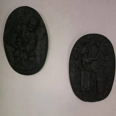 Pair of vintage black oval relief wall plaques depicting pastoral figures, mounted on a white textured wall.