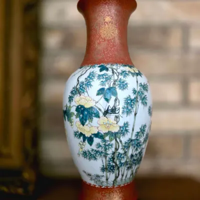 Chinese famillle rose porcelain vase featuring painted floral and bamboo motifs with gilt-accented rust red borders on the neck and base.