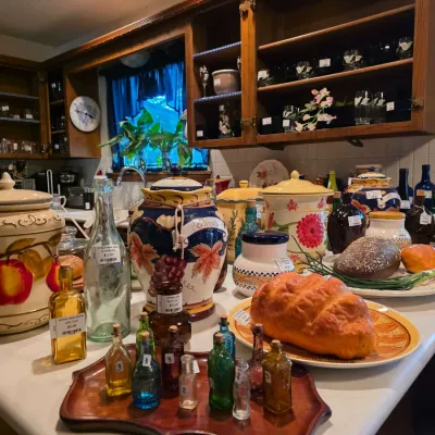 Collection of decorative ceramic cookie jars, faux bread displays, and various colored glass bottles arranged on a kitchen counter.