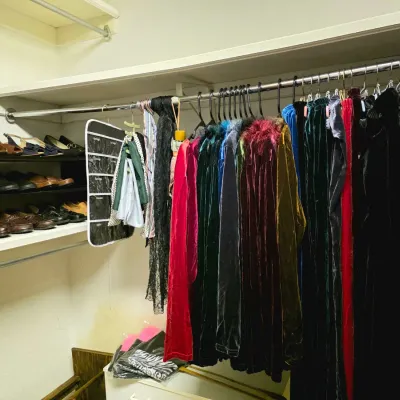 Walk-in closet filled with vintage women's clothing, featuring velvet dresses, coats, hanging organizers, and shelves lined with shoes.