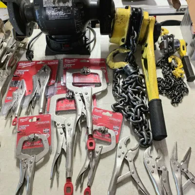 Sale Photo Thumbnail #35: Assortment of workshop tools including a bench grinder, a yellow chain hoist, and various Milwaukee locking pliers and C-clamps.