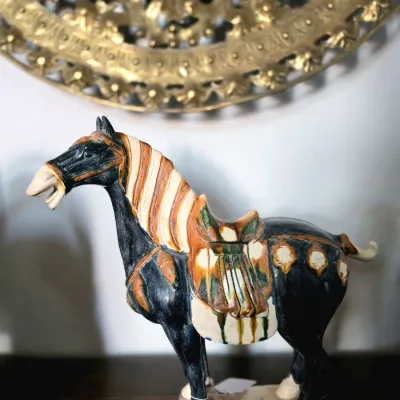 Tang Dynasty style glazed ceramic horse figurine featuring tri-color sancai glaze details on a black body.