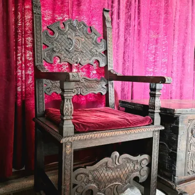 Sale Photo Thumbnail #15: Ornate Gothic Revival style carved oak armchair featuring a high back with intricate relief carvings, a red velvet seat cushion, and detailed stretchers.