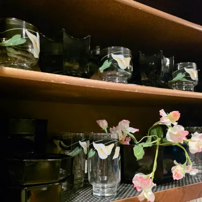 Collection of vintage glassware featuring painted calla lily motifs alongside black glass dishes arranged on cabinet shelves.