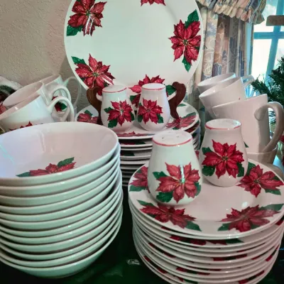 Large holiday dinnerware set decorated with red poinsettias and green leaves, including plates, bowls, mugs, a platter, and salt and...
