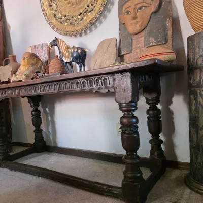 Sale Photo Thumbnail #46: Antique Spanish-style carved oak trestle table featuring heavy turned legs and a decorative carved apron, styled with various global artifacts and sculptures.