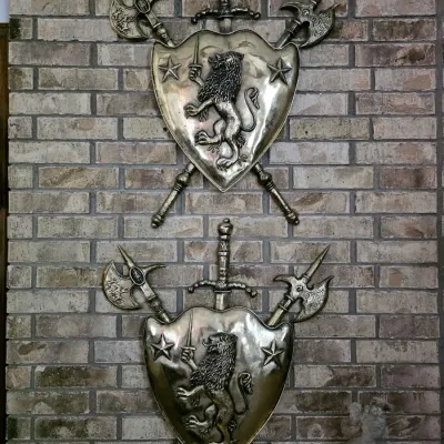 Sale Photo Thumbnail #33: Pair of vintage brass-finished medieval-style wall plaques, each featuring a shield with a rampant lion motif, flanked by crossed halberds and a central sword.