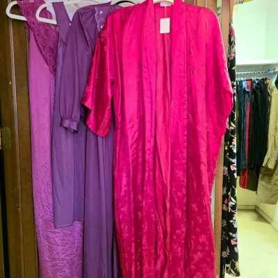 Collection of vintage women's sleepwear and robes hanging on a door rack, including a bright fuchsia jacquard kimono-style robe and...