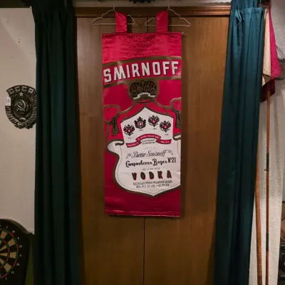 Sale Photo Thumbnail #23: Vintage Smirnoff Vodka fabric banner hanging on a closet door, alongside a metal "Old London Road" sign and a Soviet CCCP emblem.