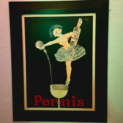 Framed vintage-style advertising poster for Pernis Super Anis, featuring a whimsical illustration of a dancer pouring a drink, set in a...