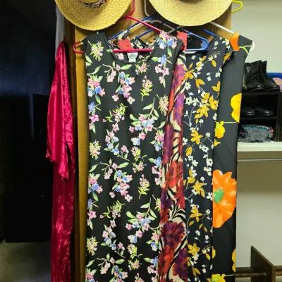 Collection of women's floral print sleeveless maxi dresses hanging on plastic hangers alongside two straw sunhats.
