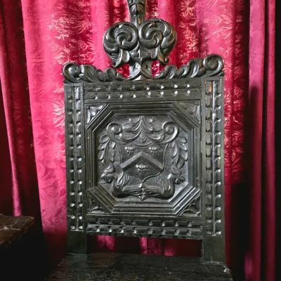 Sale Photo Thumbnail #12: Antique dark-stained oak hall chair featuring an intricately carved backrest with a central crest, scrollwork, and a prominent finial.