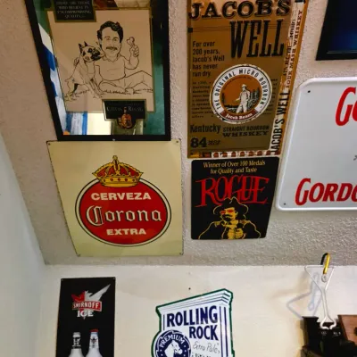 Sale Photo Thumbnail #21: Collection of vintage bar signs and mirrors, including a Jacob's Well Whiskey tin sign, a Corona Extra sign, a Rolling Rock sign, and a Smirnoff Ice poster.