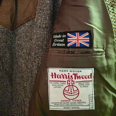 Interior lining and authentic tags of a vintage Harris Tweed wool jacket, featured alongside a 'Made in Great Britain' patch.