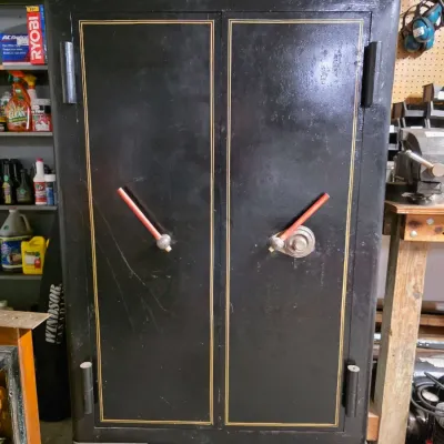 Large vintage black iron floor safe featuring double doors, gold pinstriping, and heavy-duty casters.